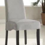 A grey velvet upholstered dining chair with a flared back and black legs.