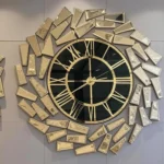An oversized gold wall clock with a black face and golden mirrored panels in an abstract geometric design.