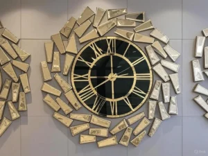 An oversized gold wall clock with a black face and golden mirrored panels in an abstract geometric design.