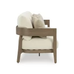 Side profile of Amos outdoor sofa showing curved wood-look armrest, thick cream cushion, and textured throw pillow detail