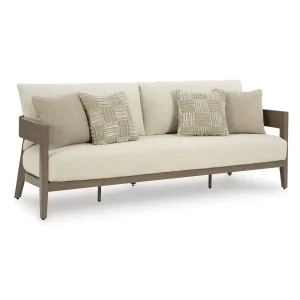 Three-quarter angle view of Amos outdoor sofa showing wood-look armrest, cream cushion depth, and decorative throw pillows