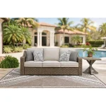 Antalya beige outdoor sofa styled on poolside patio with end table, outdoor rug and tropical landscaping in background