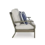 Side profile of Milas beige outdoor loveseat showing wood-look armrest, thick beige cushion, and blue striped throw pillow
