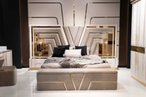 V Luxury Queen Bed with gold mirrored headboard and taupe micro velvet upholstery, shown with matching storage bench and stylish throw pillows.
