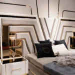 Close-up detail of the V Luxury Bed headboard and bedside table, highlighting the mirrored accents, gold trim, integrated lighting, and plush taupe velvet fabric.