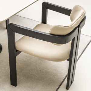 Modern dining chair with sleek black wooden arms and legs, set against a luxury dining room interior.