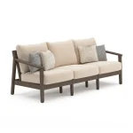 Three-quarter angle view of Patara acacia outdoor sofa showing armrest design, wood frame finish, and plush beige cushion depth
