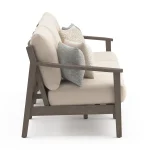 Side profile view of Patara acacia wood outdoor sofa showing dark brown armrest, thick beige cushions, and sturdy angled legs on white background