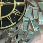 A gold wall clock with a black face and golden mirrored panels in an abstract geometric design.
