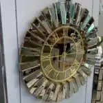 A large wall clock with a bronze mirrored frame, a black face, and Roman numeral wall clock design.
