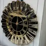An oversized wall clock with a bronze mirrored frame, a black face, and Roman numeral wall clock design.
