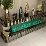 A 79-inch bronze mirrored TV stand with a green-glowing electric fireplace and decorative items on top.
