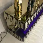 n angled close-up of a bronze mirrored TV stand with a purple electric fireplace glow and decorative objects.