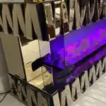 A side-angle close-up of the glowing purple fireplace in the Bronze Mirrored TV Stand with the remote control visible.