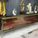A close-up of a bronze mirrored TV stand's electric fireplace with a red glow and the remote control on top.