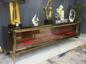 A close-up of a bronze mirrored TV stand's electric fireplace with a red glow and the remote control on top.