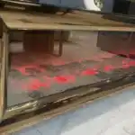 A bronze curved mirrored TV stand with an electric fireplace glowing red, decorated with gold and white accents.