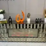 A bronze mirrored TV stand with a purple glowing electric fireplace and a remote control on the bottom shelf.