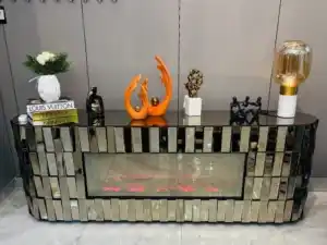 A bronze mirrored TV stand with a purple glowing electric fireplace and a remote control on the bottom shelf.