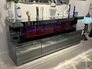 A close-up of a dark gray mirrored TV stand's electric fireplace with a red glow and the remote control on top.