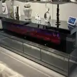 A dark gray mirrored fireplace TV stand with its four drawers pulled out, showing the storage space inside.