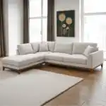 A stylish Watton Mid-Century Modern sectional sofa in light gray chenille fabric, featuring a left chaise and warm walnut tone wood trim, set in a bright, contemporary living room.