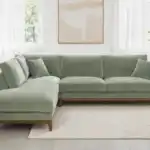 A contemporary Watton Mid-Century Modern sectional sofa in olive green chenille fabric, featuring a left chaise and warm walnut tone wood trim, set in a bright living room.