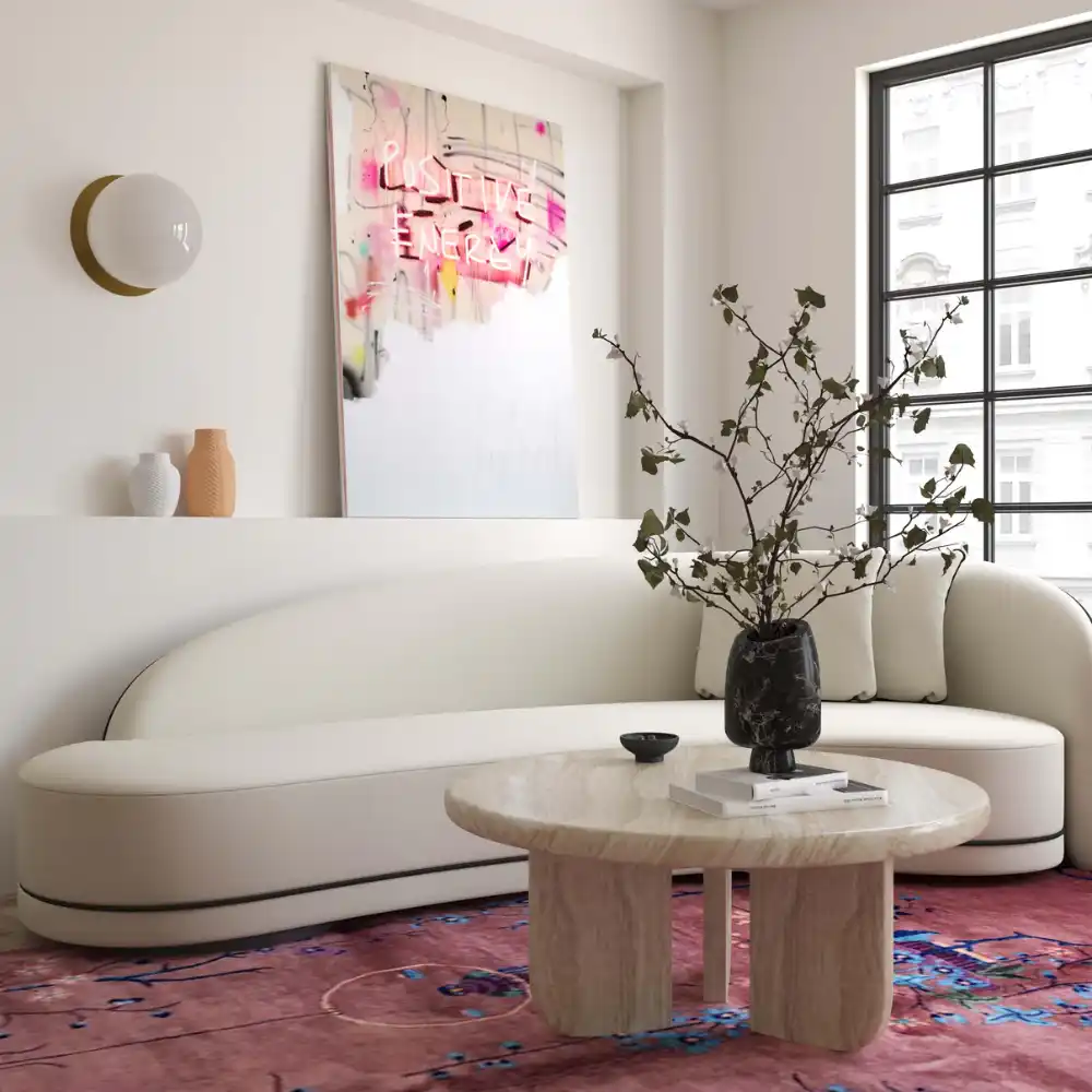 Patrizia 36-inch Faux Travertine Concrete Indoor/Outdoor Round Coffee Table, modern curved sofa, pink floral rug, and contemporary artwork in a luxury living room setting.