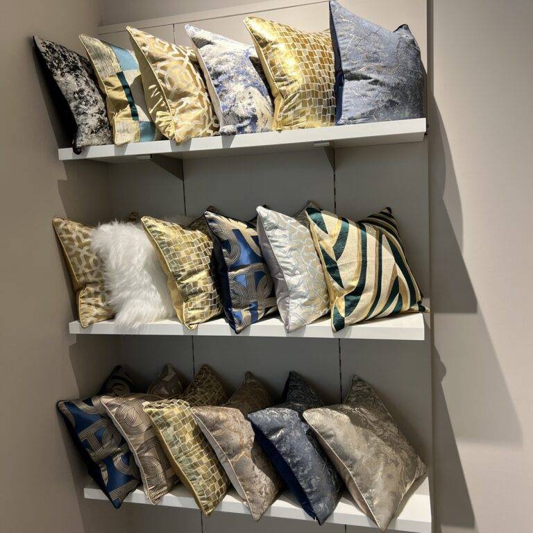A display of luxurious modern throw pillows in various colors and patterns on white shelves.