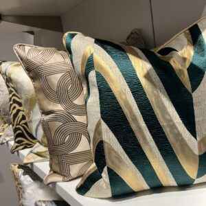 A display of luxurious modern throw pillows in various colors and patterns on white shelves.