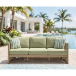 Gumbet 3 seater green outdoor sofa styled on poolside patio with blue leaf-patterned rug and tropical landscaping