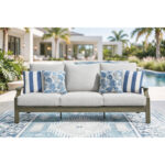 Milas beige patio sofa styled on outdoor rug beside pool with modern home and palm trees in background