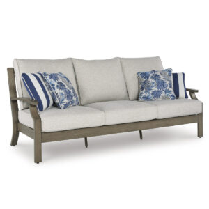 Three-quarter angle view of Milas beige aluminum outdoor sofa showing wood-look armrest, beige cushion depth, and blue decorative pillows