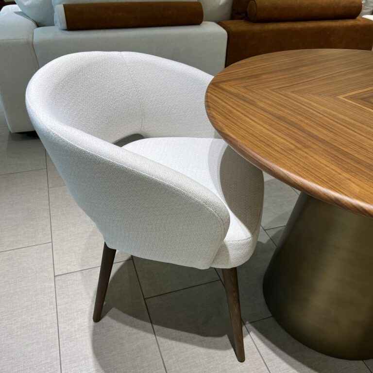 Touch dining chair with walnut wooden legs and white fabric upholstery next to a round dining table with a walnut finish.