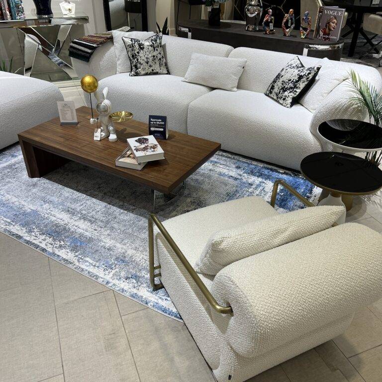 Modern European living room setup featuring a white sectional sofa, a wooden coffee table, and a white armchair with gold accents.